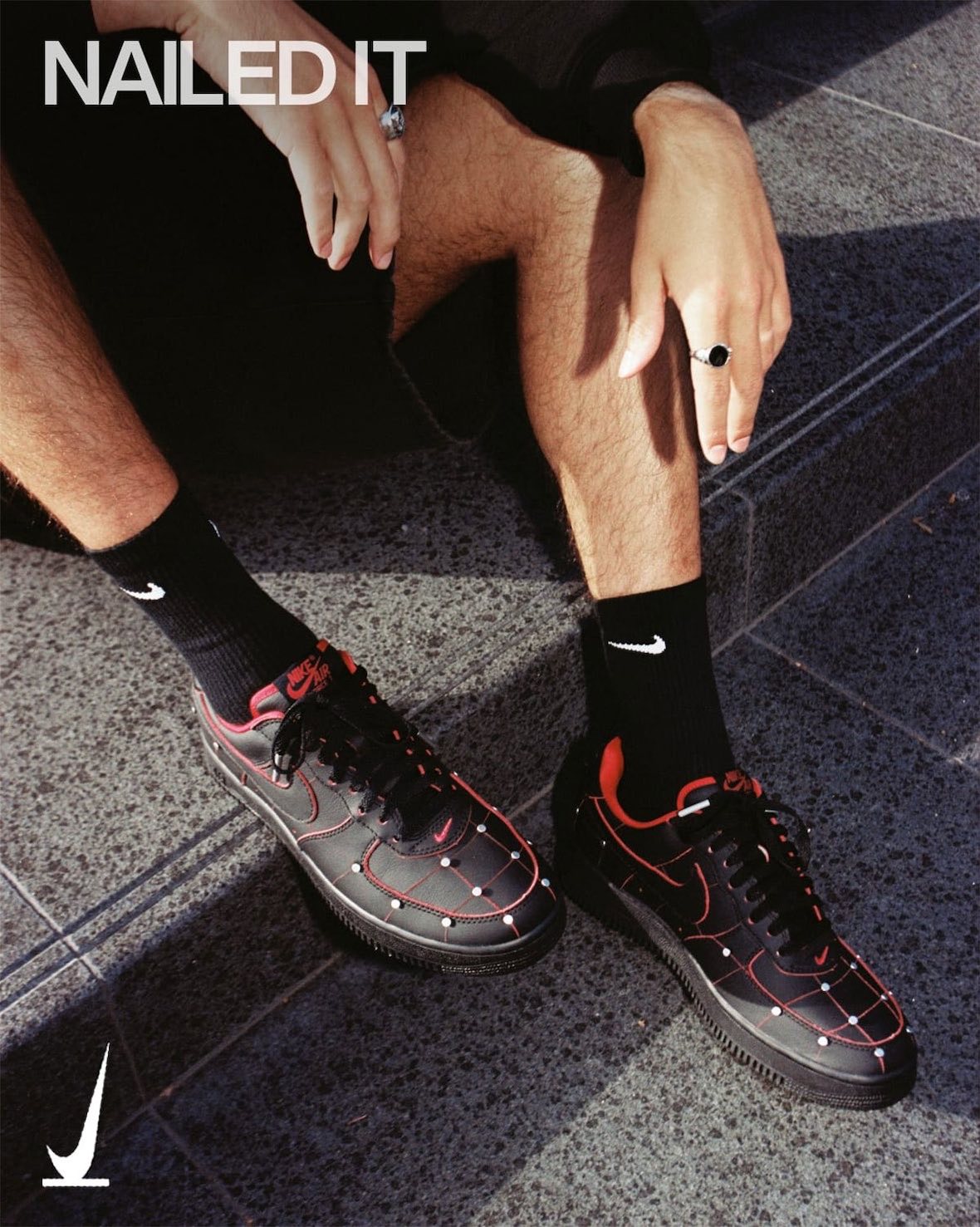 Persona sentada en un escalón con el Nike Air Force 1 '01 Nightmare puesto, con medias negras Nike, en la imagen de campaña con la frase Nailed It arriba