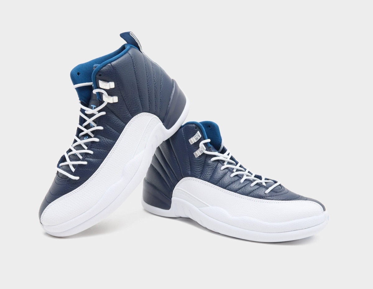 Par de Air Jordan 12 Obsidian apoyados uno junto al otro sobre fondo gris claro, con el cuero azul marino, la puntera blanca texturada y el forro azul en el cuello