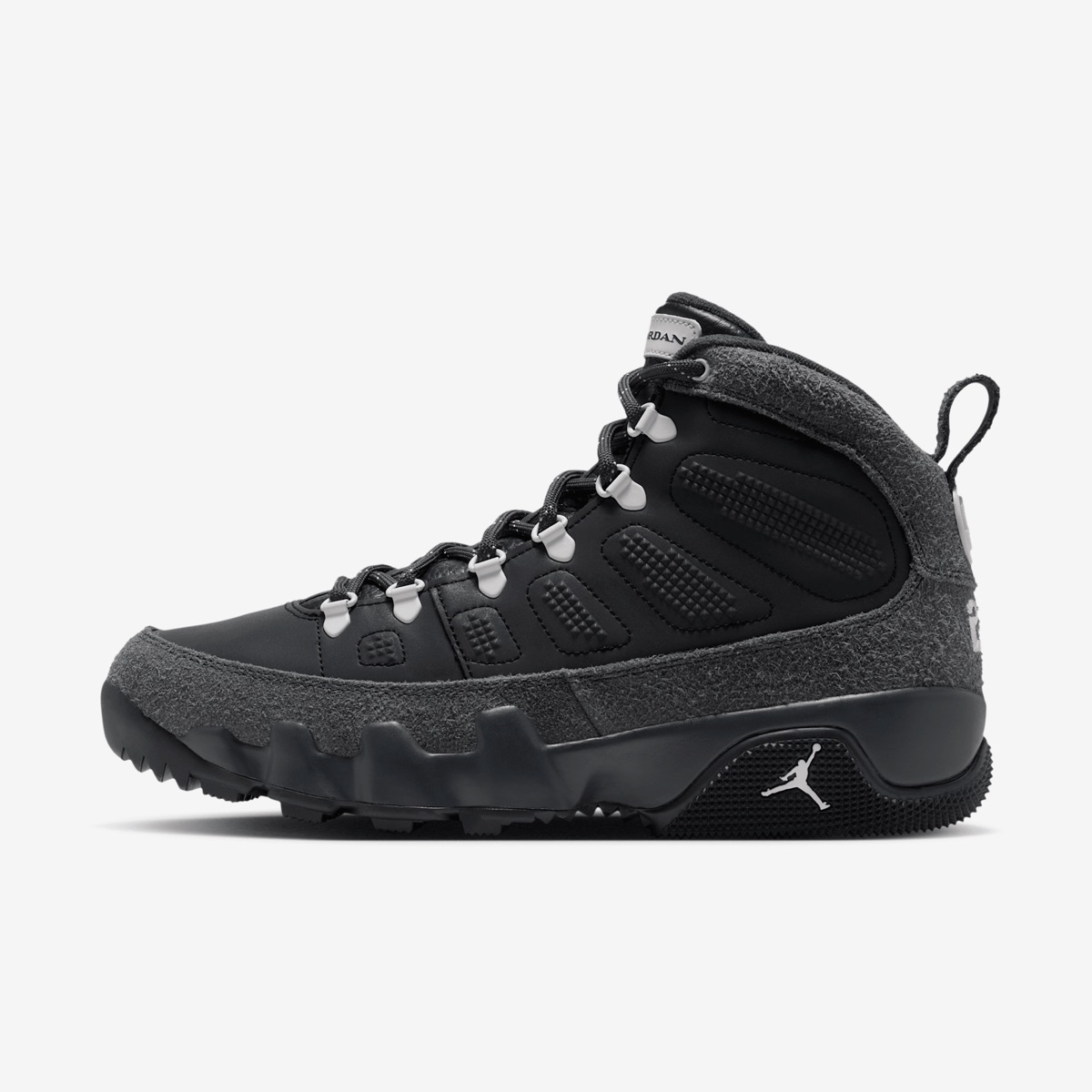 Air Jordan 9 Retro Boot NRG Anthracite de perfil sobre fondo blanco, con el cuerpo de cuero negro y sus relieves, gamuza gris oscura en la base, el cuello y el talón, ojales de metal con terminales grises, tira para calzarse en el talón y suela negra con el Jumpman blanco