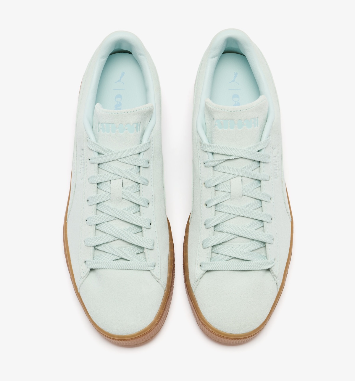 Vista superior del par PUMA Suede Sea Glass de Daniëlle Cathari, con la marca Cathari grabada en la lengüeta, cordones planos verde agua y plantilla celeste con los logos de PUMA y Cathari