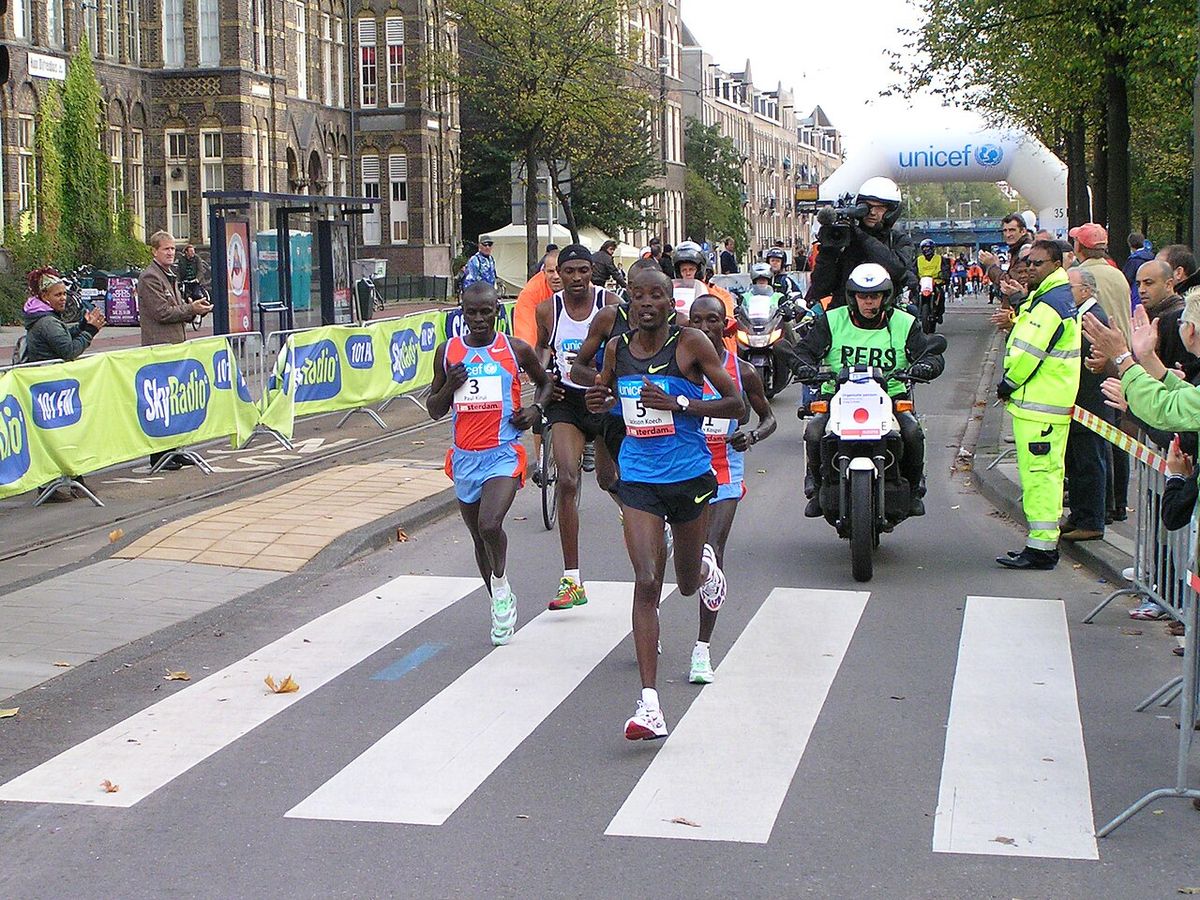 Foto de archivo: el grupo de punta del Maratón de Ámsterdam pasa por una calle con edificios de ladrillo, escoltado por motos y con público detrás de las vallas