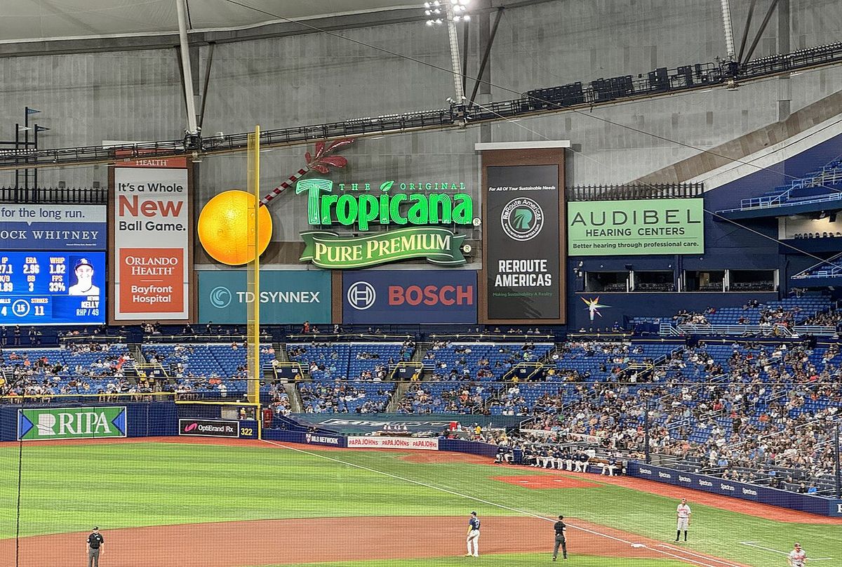 Foto de archivo: el jardín izquierdo de Tropicana Field, con el cartel luminoso de Tropicana y una naranja gigante sobre la tribuna, el poste de foul amarillo y los jugadores en el campo durante un partido de los Rays