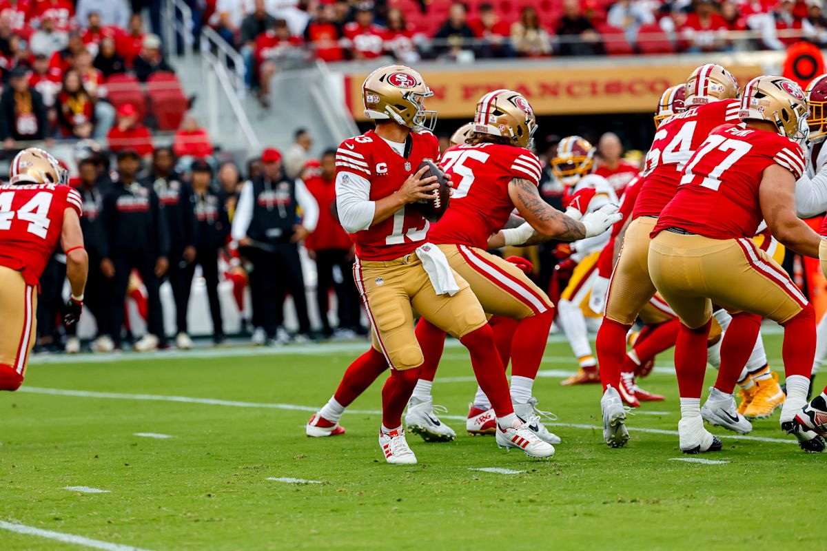 Brock Purdy, con la camiseta roja número 13, retrocede para lanzar protegido por su línea ofensiva ante los Commanders en el Levi's Stadium