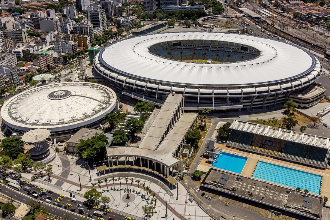 Vista aérea del estadio Maracaná de Río de Janeiro, con su techo blanco circular, rodeado de edificios, un gimnasio y un parque acuático con dos piletas