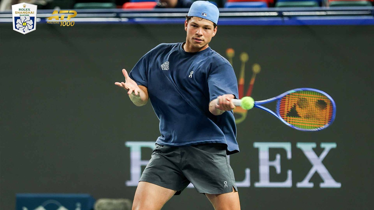 Ben Shelton, con remera azul, short gris y gorra celeste, pega un drive durante un entrenamiento en el Qi Zhong Stadium, con el logo del Rolex Shanghai Masters arriba a la izquierda
