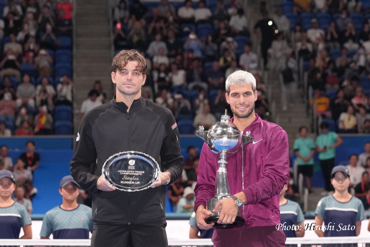 Foto de archivo: Carlos Alcaraz, con campera bordó, sostiene el trofeo de campeón del Japan Open 2025 junto a Taylor Fritz, de negro, con la bandeja de subcampeón