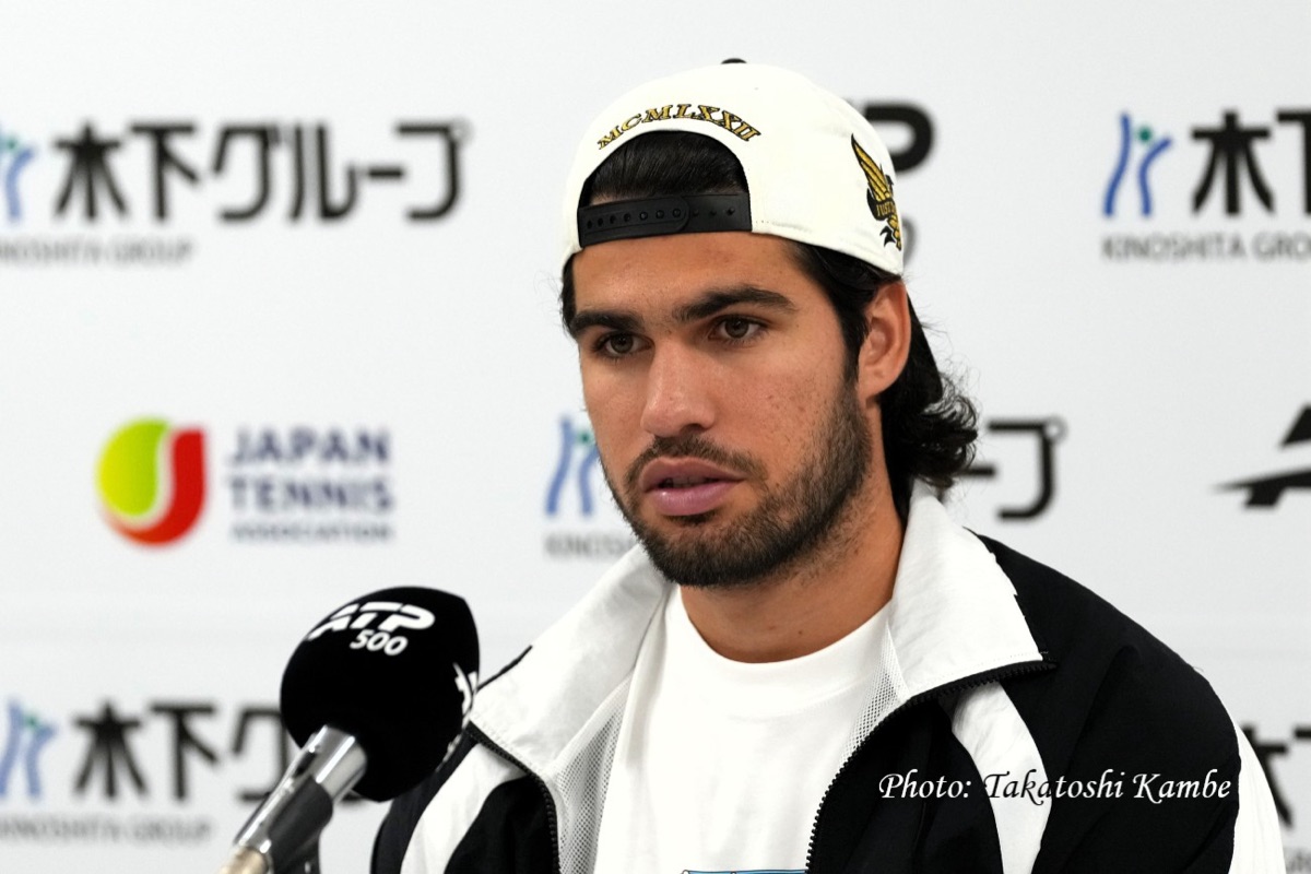 Carlos Alcaraz, con gorra blanca hacia atrás y campera blanca y negra, habla en conferencia de prensa frente al micrófono del ATP 500 en el Japan Open
