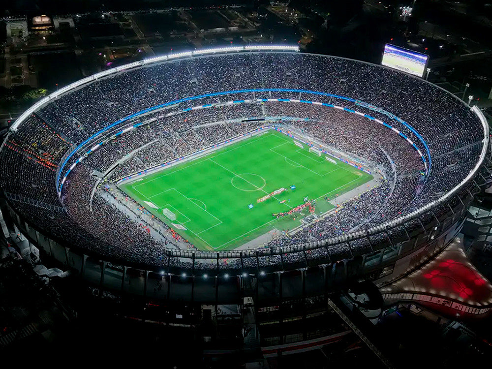 Vista aérea nocturna del Estadio Monumental con las tribunas llenas y el campo de juego iluminado, en una foto de archivo de la AFA
