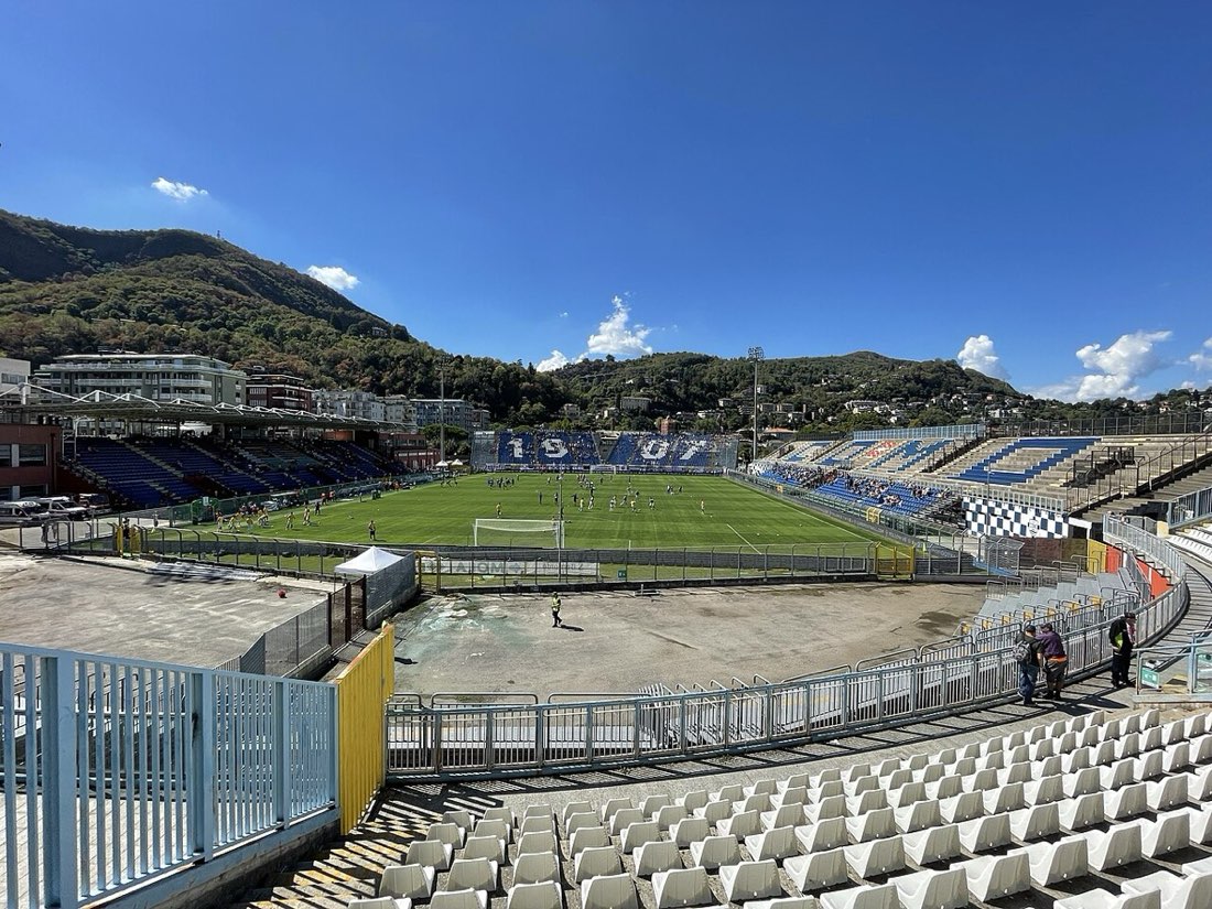 Las tribunas y el campo de juego del estadio Giuseppe Sinigaglia de Como, con los cerros de fondo y el cielo azul; foto de archivo de septiembre de 2022 (foto: Vale93b, Wikimedia Commons, licencia CC BY-SA 4.0)
