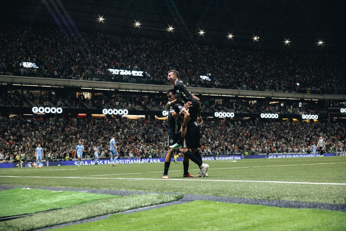Dos jugadores de Atlético Mineiro, uno subido a la espalda del otro, festejan un gol junto a la línea de fondo mientras los futbolistas de Montevideo City Torque, de celeste, vuelven al medio con la Arena MRV llena de fondo (foto: Pedro Souza / prensa oficial de Atlético Mineiro)
