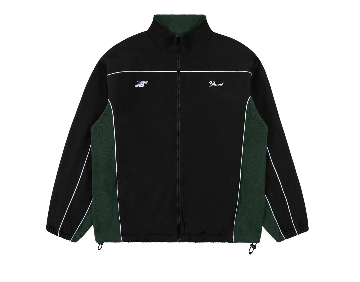 Campera de Grand Collection y New Balance Numeric sobre fondo blanco, de nylon negro con laterales de polar verde bosque, vivos blancos, cierre al frente y los logos NB# y Grand bordados en blanco en el pecho