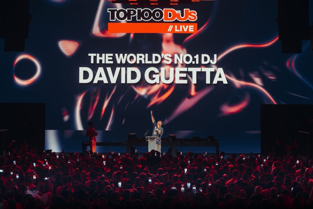 Foto oficial de la ceremonia en [UNVRS], Ibiza: David Guetta levanta el brazo en un atril sobre el escenario, frente a una pantalla gigante que dice «The World's No.1 DJ David Guetta», con el público iluminado de rojo y cientos de celulares en alto