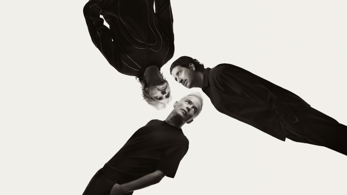 Foto de prensa en blanco y negro de The Avalanches: tres integrantes vestidos de negro, uno cabeza abajo, que se miran entre sí contra un fondo claro