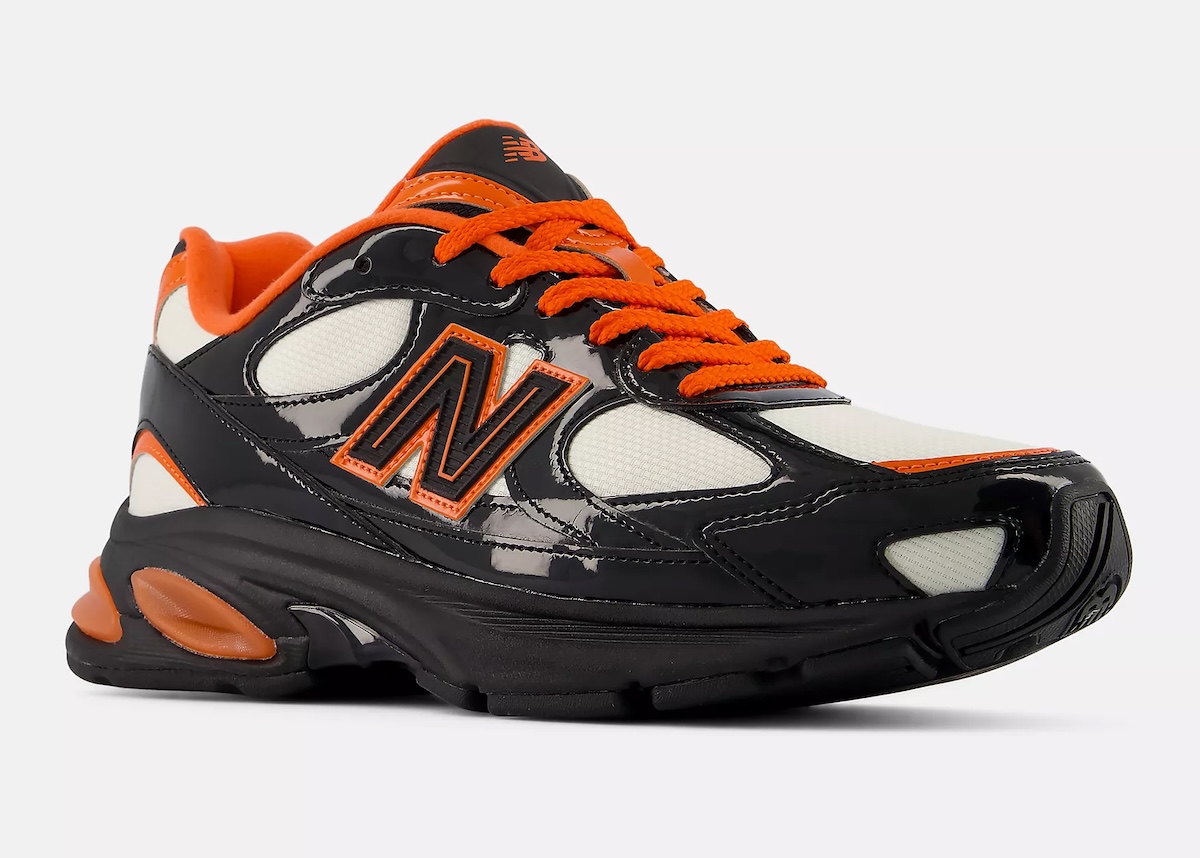 New Balance 2010 Halloween en vista tres cuartos sobre fondo gris claro, con la puntera de charol negro en primer plano, malla crema en la punta y el medio pie, logo N con borde naranja, cordones naranjas y pods naranjas en el talón