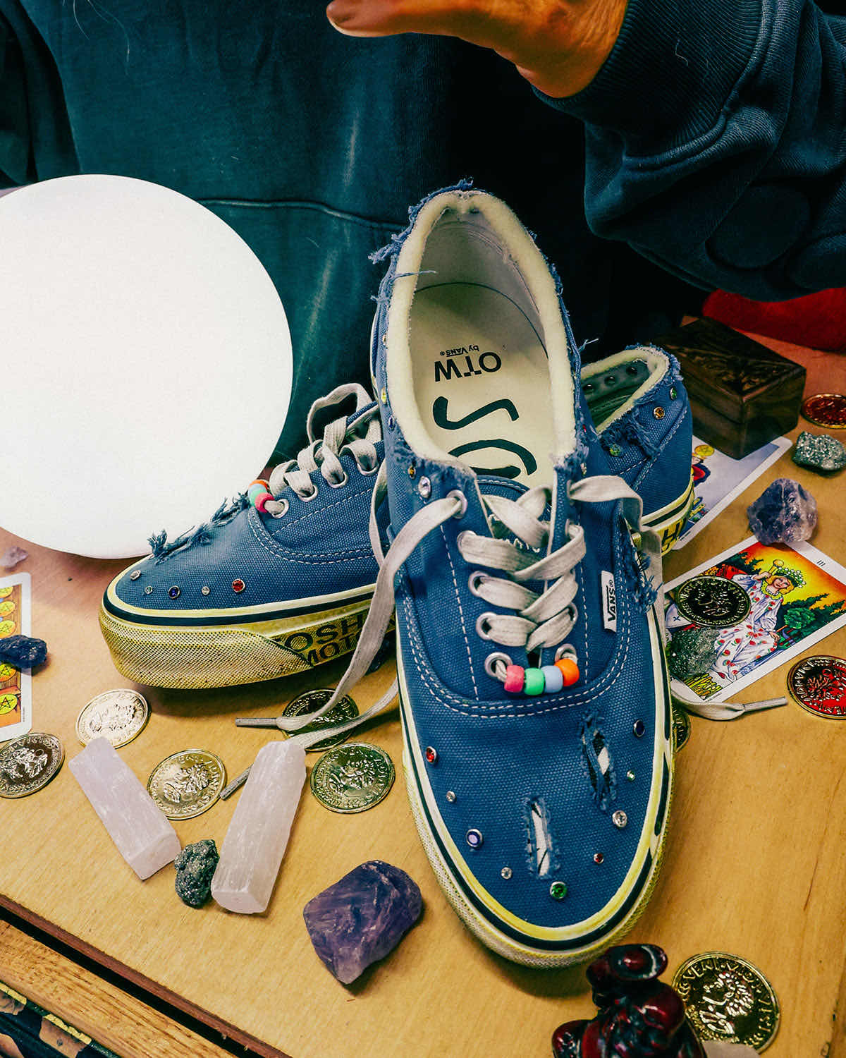Par de Satoshi Nakamoto x Vans Era 95 Lucky Charms azul con roturas en la puntera, joyas de colores y cuentas en los cordones, rodeado de cristales, monedas y cartas de tarot