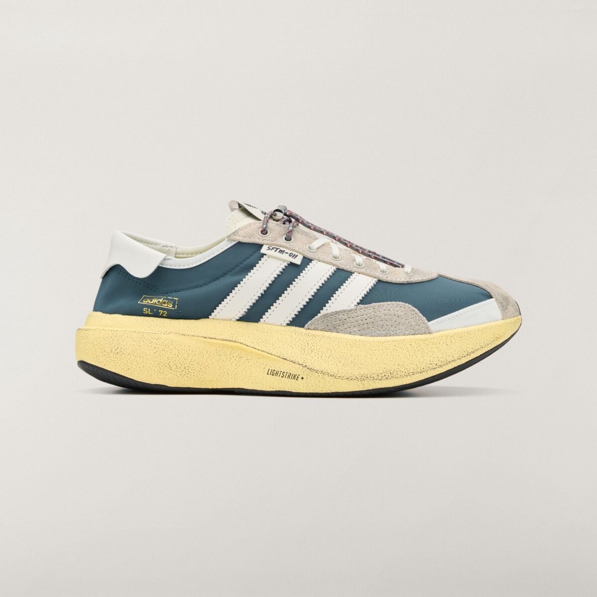 Vista lateral del adidas SL 72 PRO Wild Teal de Song for the Mute, con capellado textil verde azulado, tres tiras blancas dentadas, puntera y talón de gamuza gris, cordón con toggle, etiqueta SFTM-011 y mediasuela alta amarilla con la inscripción Lightstrike+