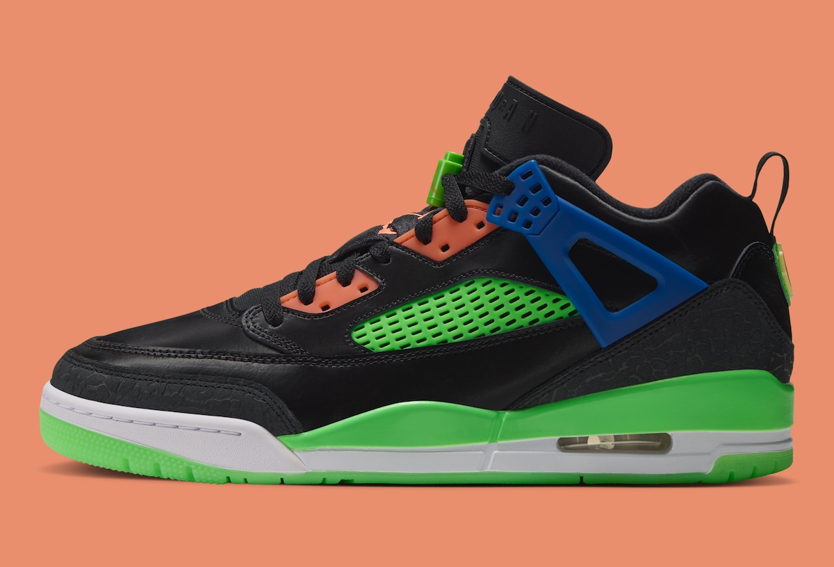 Jordan Spizike Low Jam Central de perfil sobre fondo naranja, con upper de cuero negro, red lateral verde, panel de cordones naranja, ala de cordones azul, entresuela verde y blanca con cámara de aire visible y suela verde