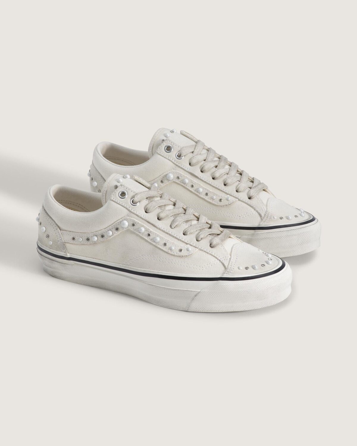 Par del Vans Old Skool 36 Pearlized Marshmallow White en vista de tres cuartos, con perlas y strass en el Sidestripe, la puntera y el talón, y la mediasuela con efecto gastado